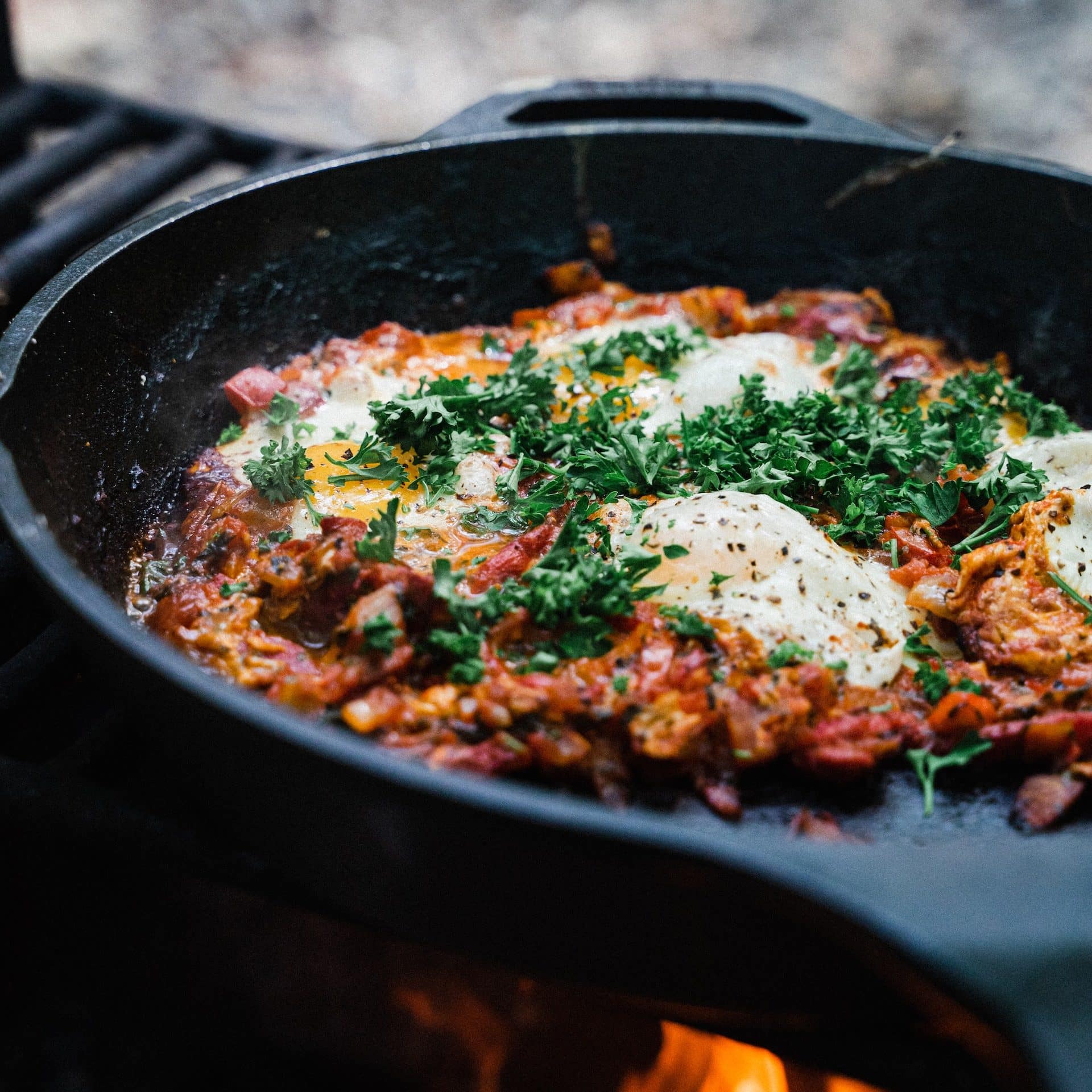 Cast iron skillet cooking food over campfire