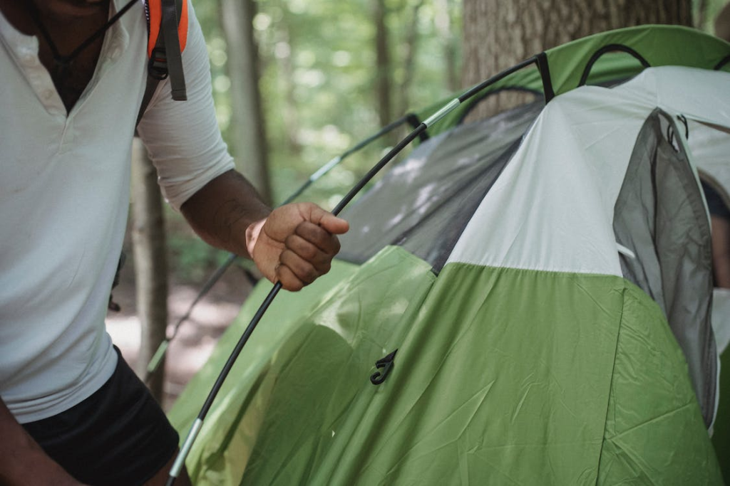 A camper arranging the poles of a green tent