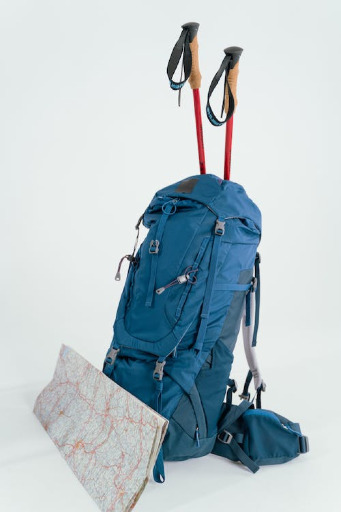 A blue hiking backpack with trekking poles and a folded map