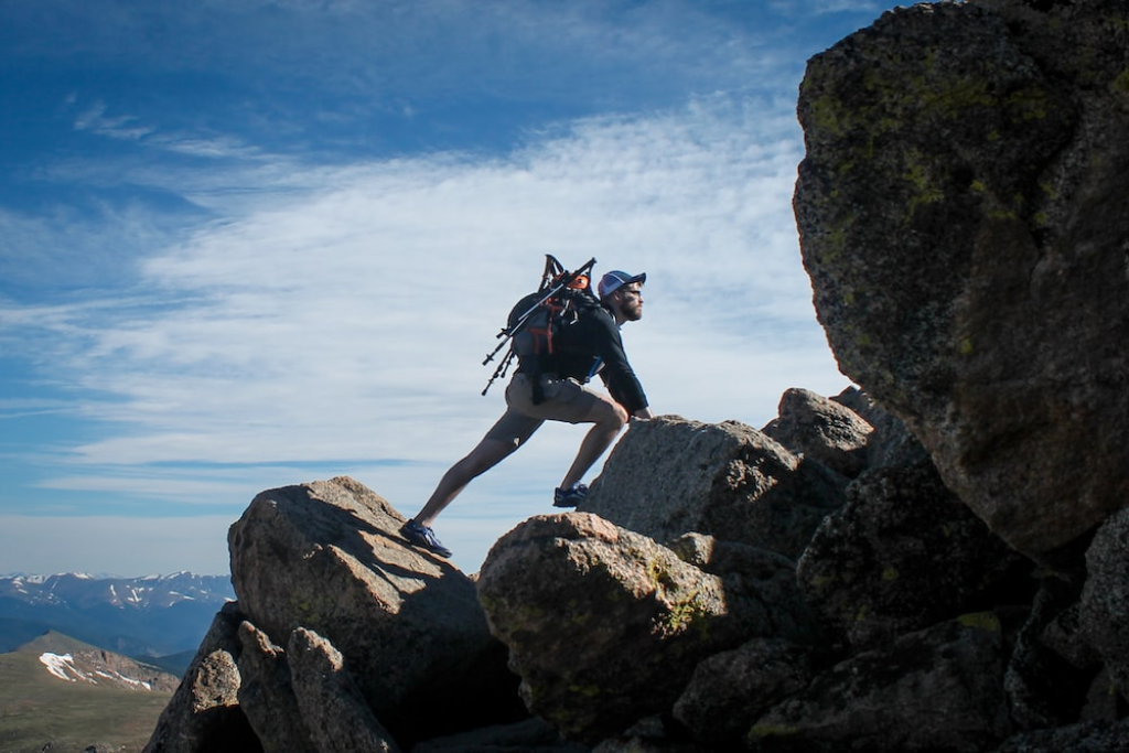 A man carrying a mountaineering backpack and trekking poles climbing large rocks