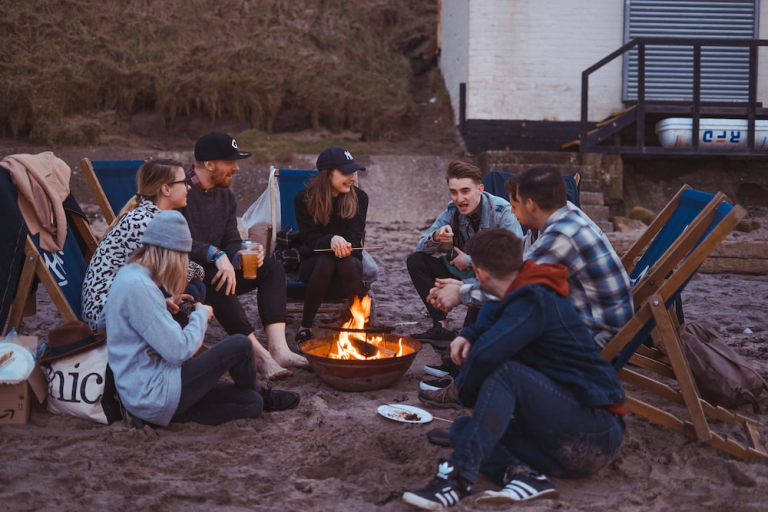 A group of people sitting around a fire pit on the beach, enjoying a cozy night under the stars.