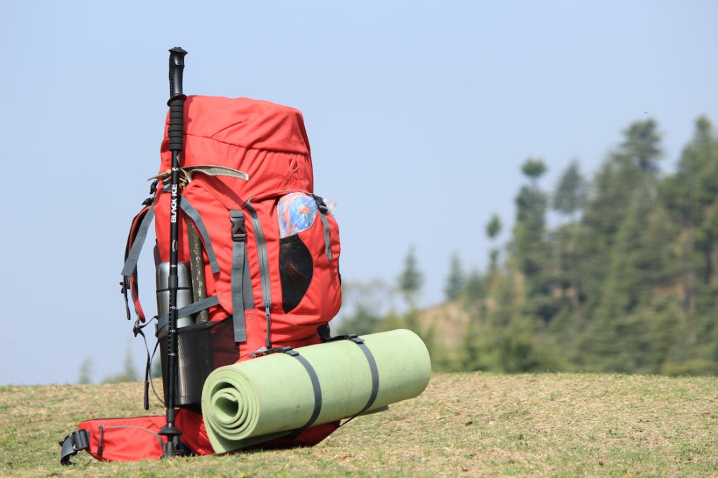 A red backpack with hiking gear, trekking poles, and a mat