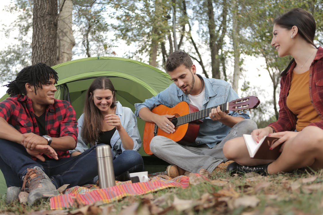 A group of friends sharing a tent while playing guitar.
