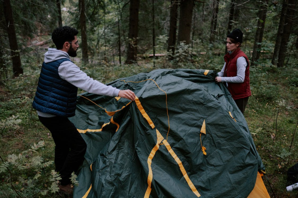 A male and a female camper setting up a grey tent in a forest