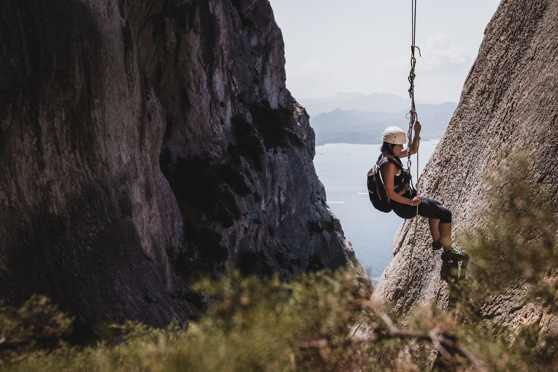 A man is scaling a cliff during mountain climbing, using a rope for support.