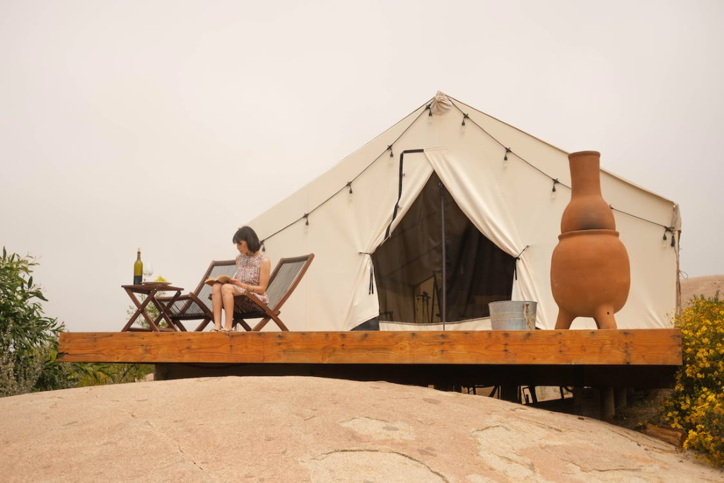 Woman reading while sitting on the deck of her luxury glamping tent