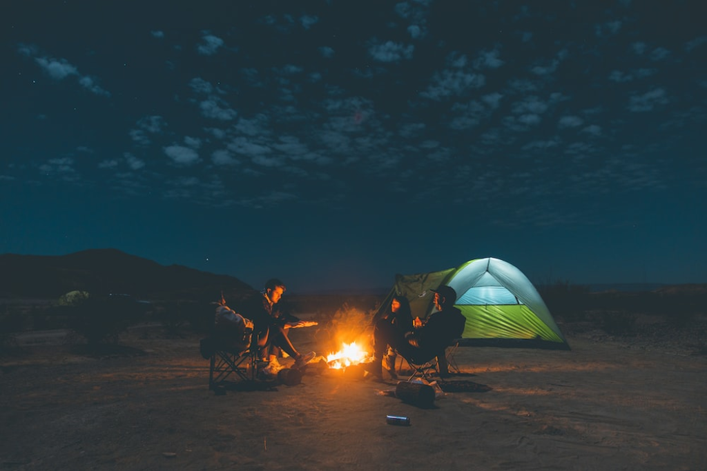 Men sitting outside their adult camping tent under the sky.