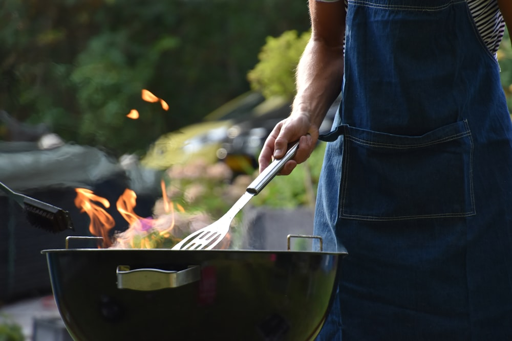 A man in a blue apron is cooking on a camping cookware bbq.