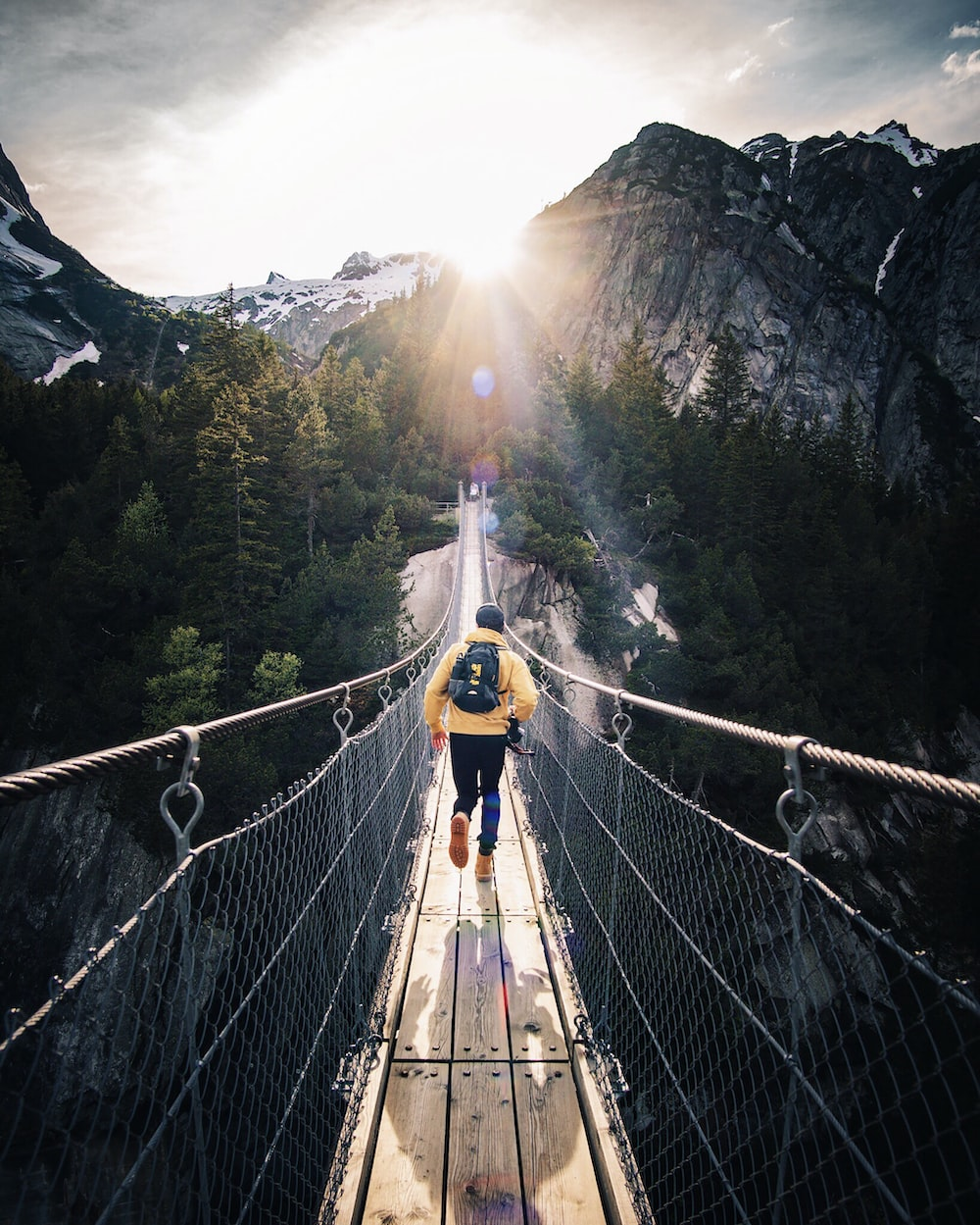 A man hiking across a suspension bridge in the mountains, exploring magnificent camping destinations along the way.