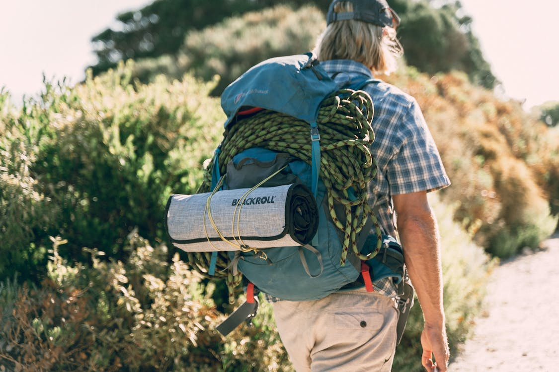 A man is walking down a path with a backpack containing groundbreaking climbing gear.