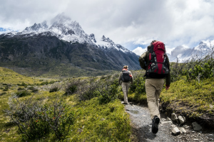 Two hikers with top hiking gear walking down a trail with mountains in the background.