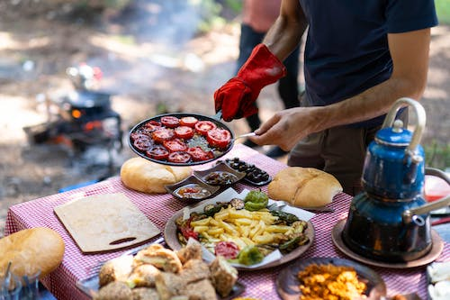 A man is cooking food while camping on a picnic table.