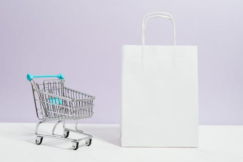 A white shopping bag is placed next to a small shopping cart.