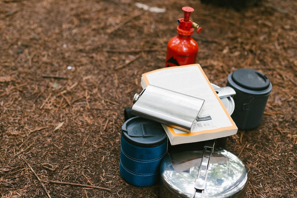 A camp stove, pots, and a book on the ground.