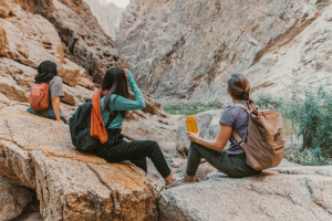 Three women sitting on rocks in a canyon with backpacks.