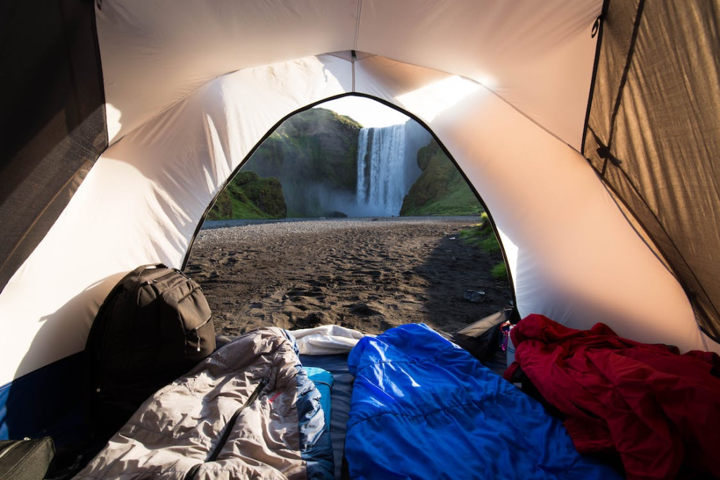 The inside of a tent with sleeping bags and a view of a waterfall.