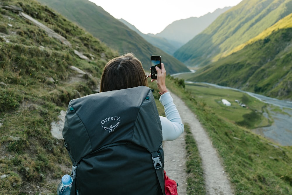 A woman taking a picture with her cell phone on a trail.